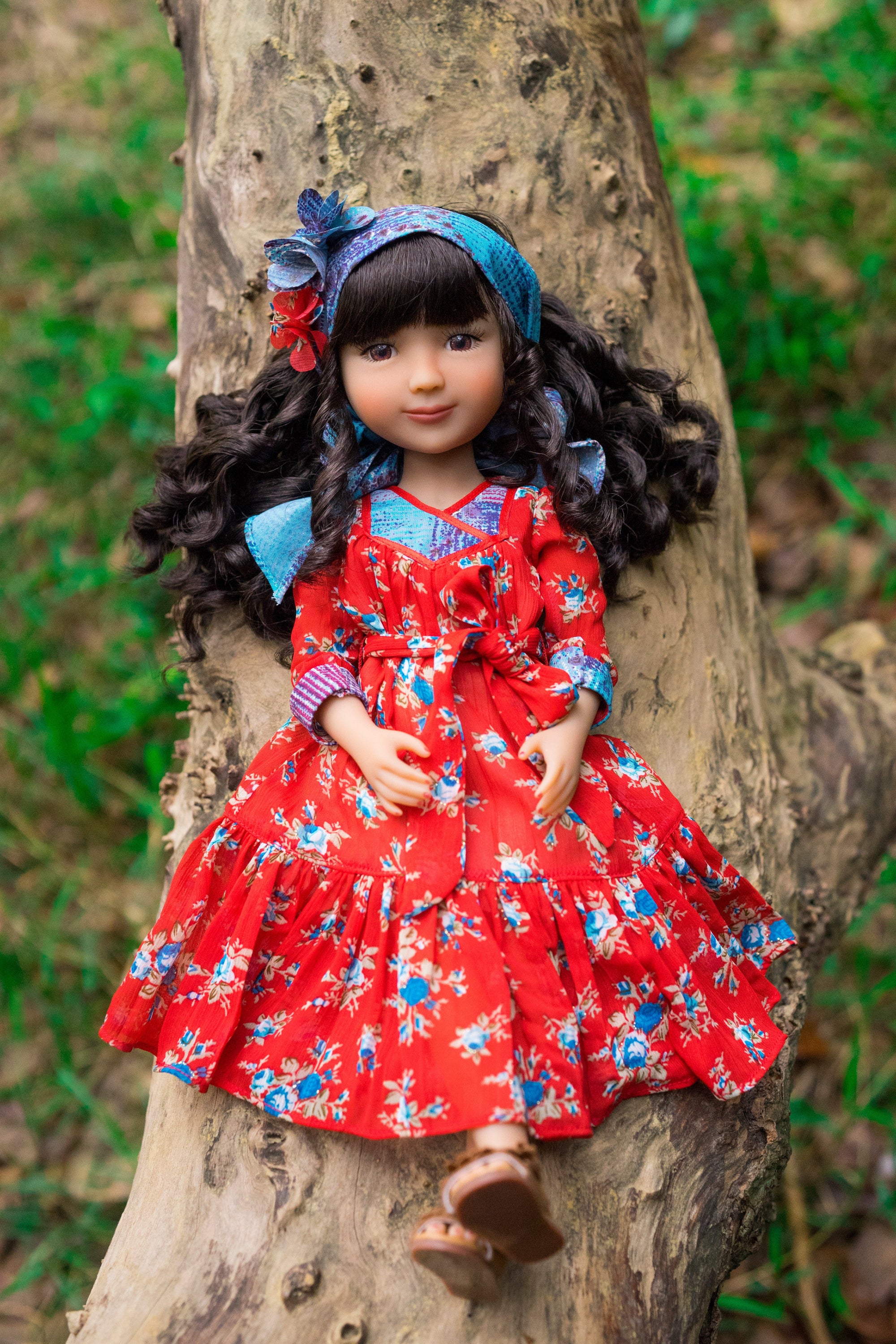 Doll in a red floral dress sitting on a tree stump in a natural setting