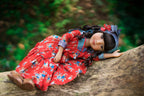 Doll in a red floral dress lying on a log with a blurred natural background