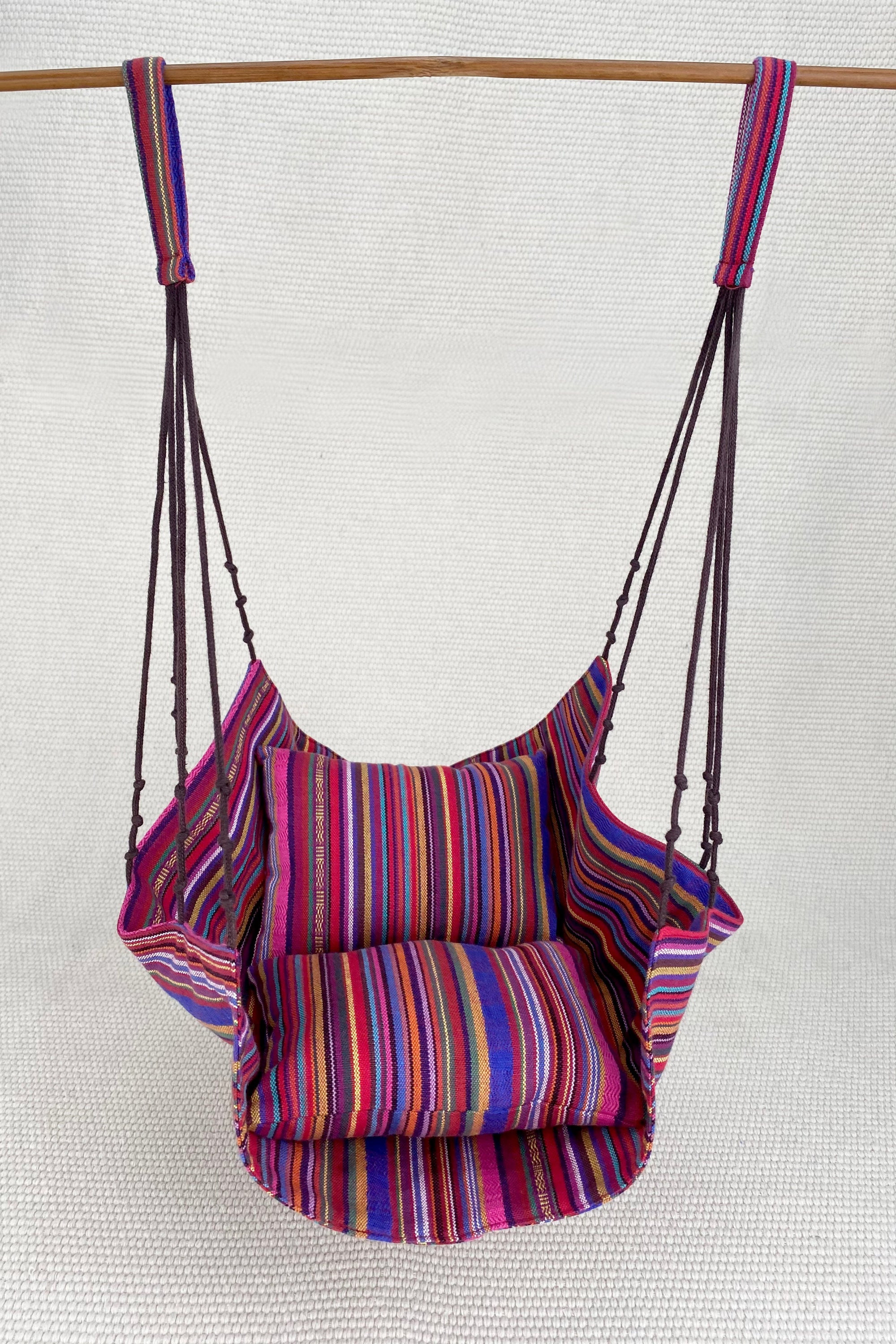 Colorful striped swing hanging on a wooden rod against a white background