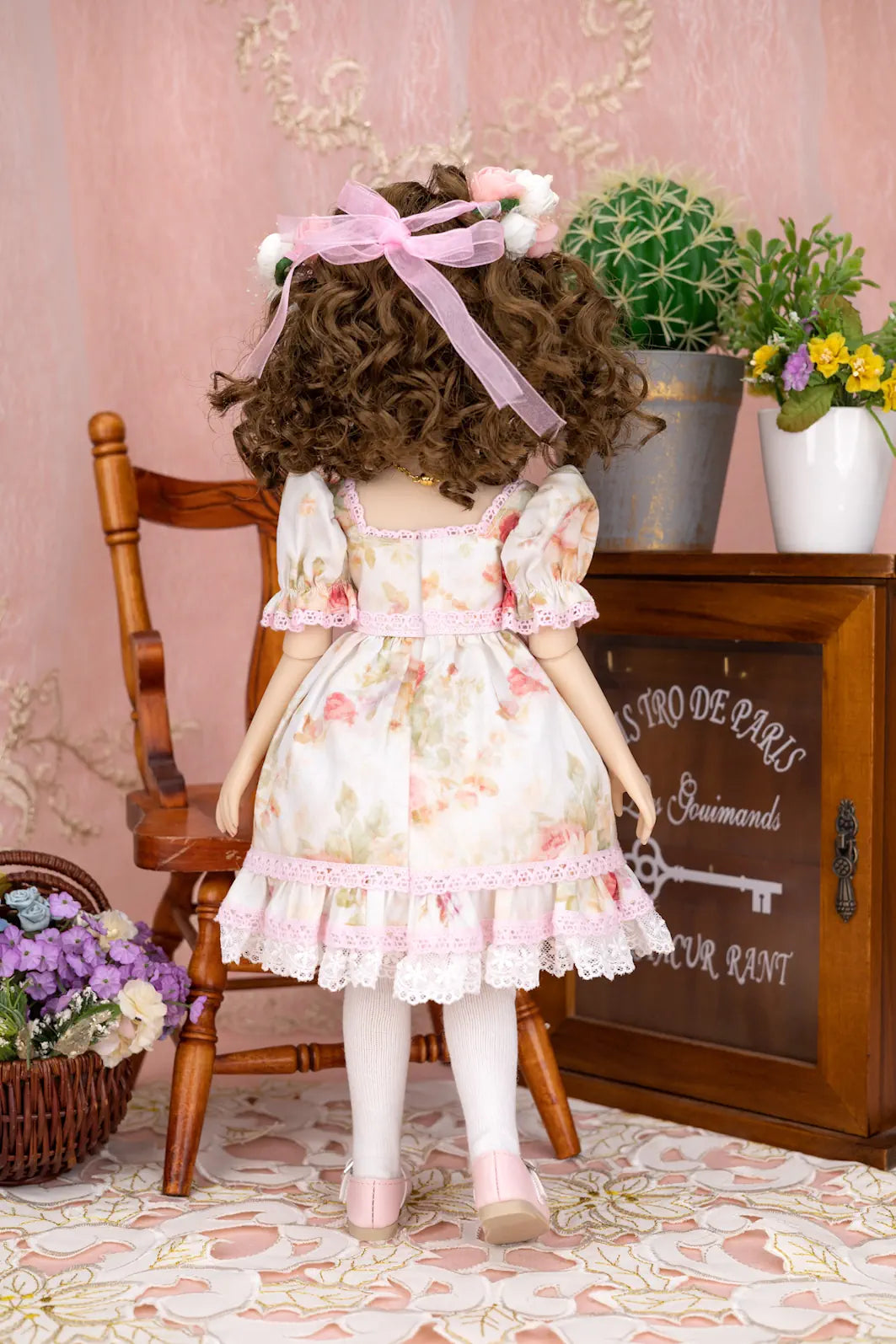 Doll in a floral dress sitting on a chair with a decorative background