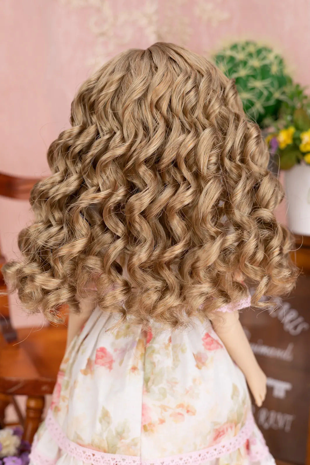 Back view of a doll with wavy blonde hair wearing a floral dress.