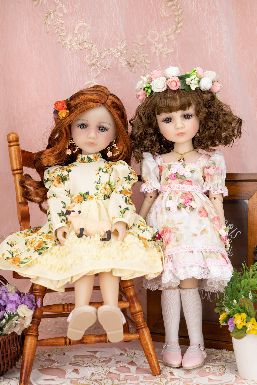 Two dolls in floral dresses sitting on a wooden chair with a decorative background.