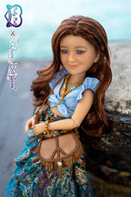 Doll with long brown hair wearing a blue top and colorful skirt, sitting on a stone surface.