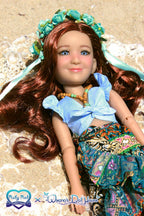 Doll with long brown hair and floral headband lying on sand, wearing a blue top and patterned skirt.