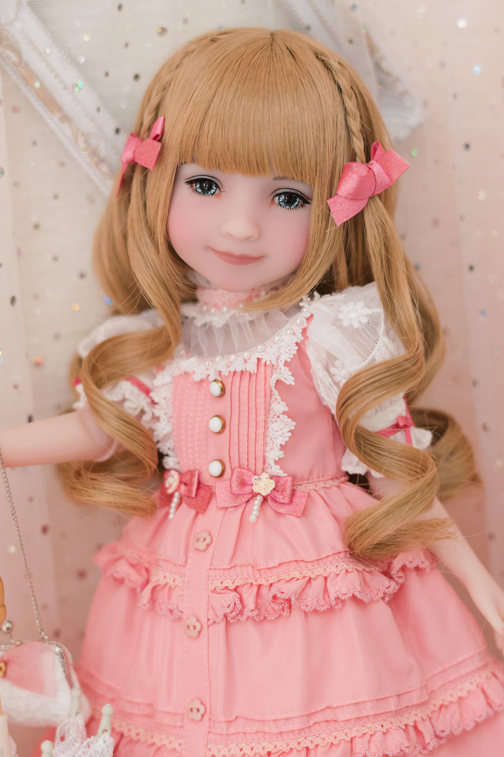 Doll with blonde hair styled in pigtails, wearing a pink dress with white lace details.