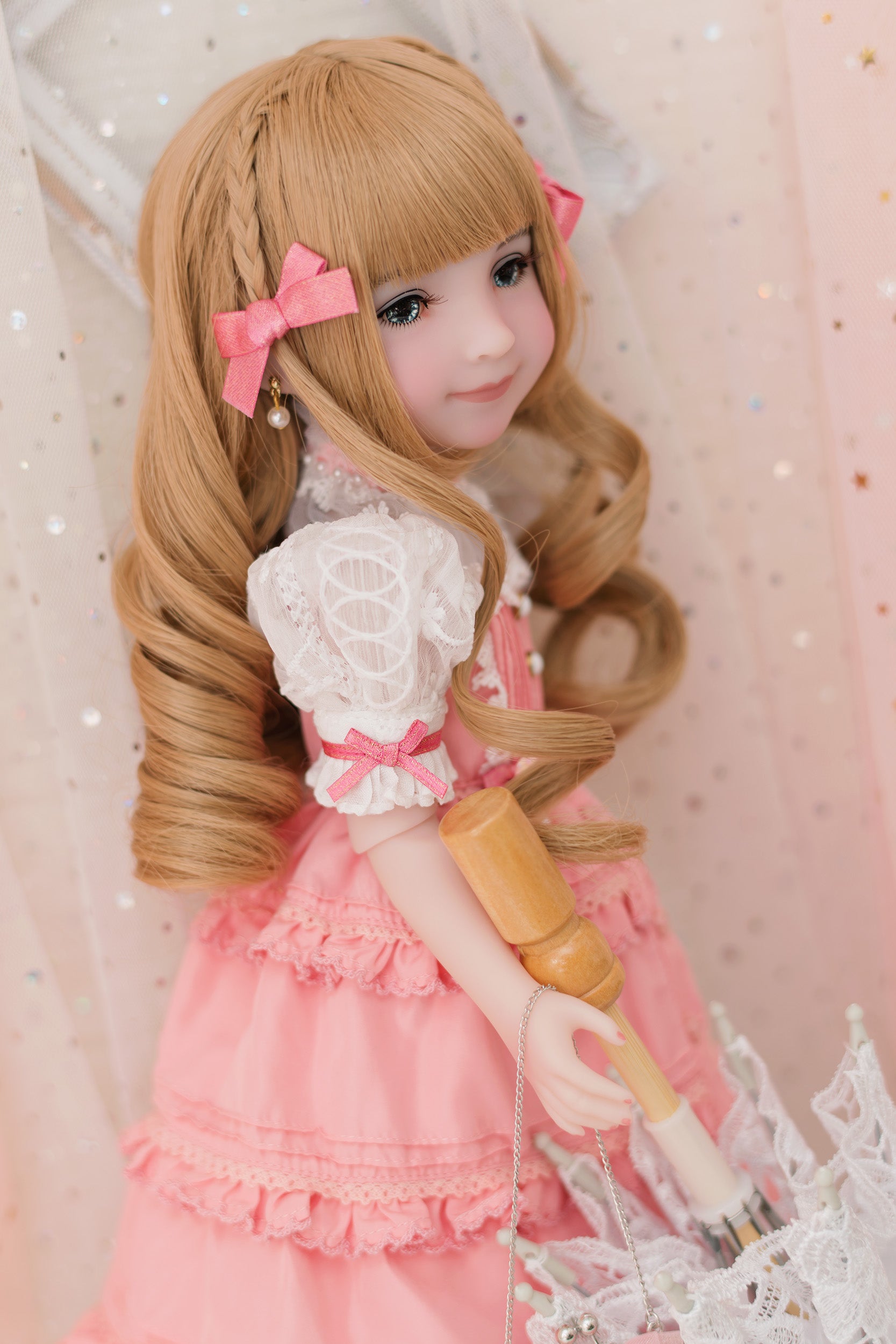 Doll with long blonde hair and a pink outfit against a soft pink background