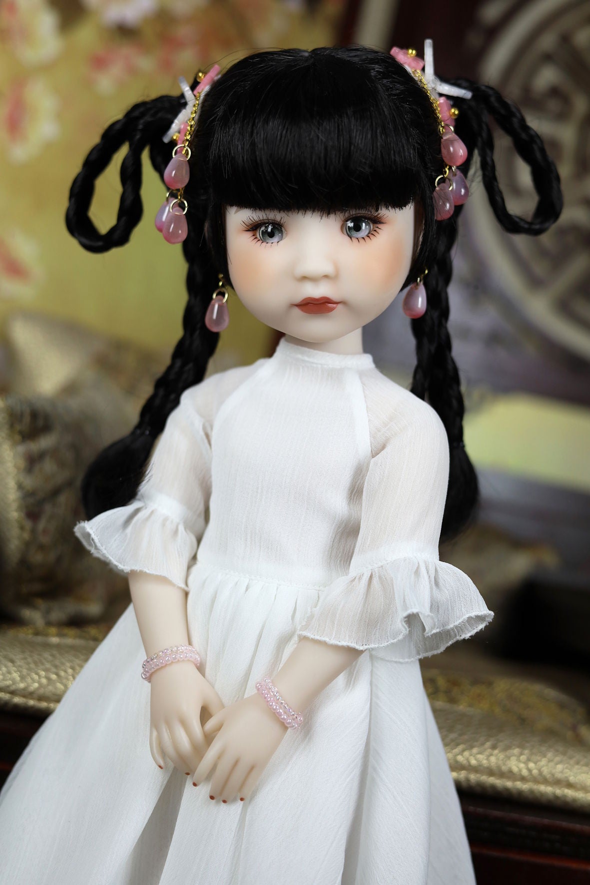 Doll with black hair styled in pigtails, wearing a white dress with ruffled sleeves.