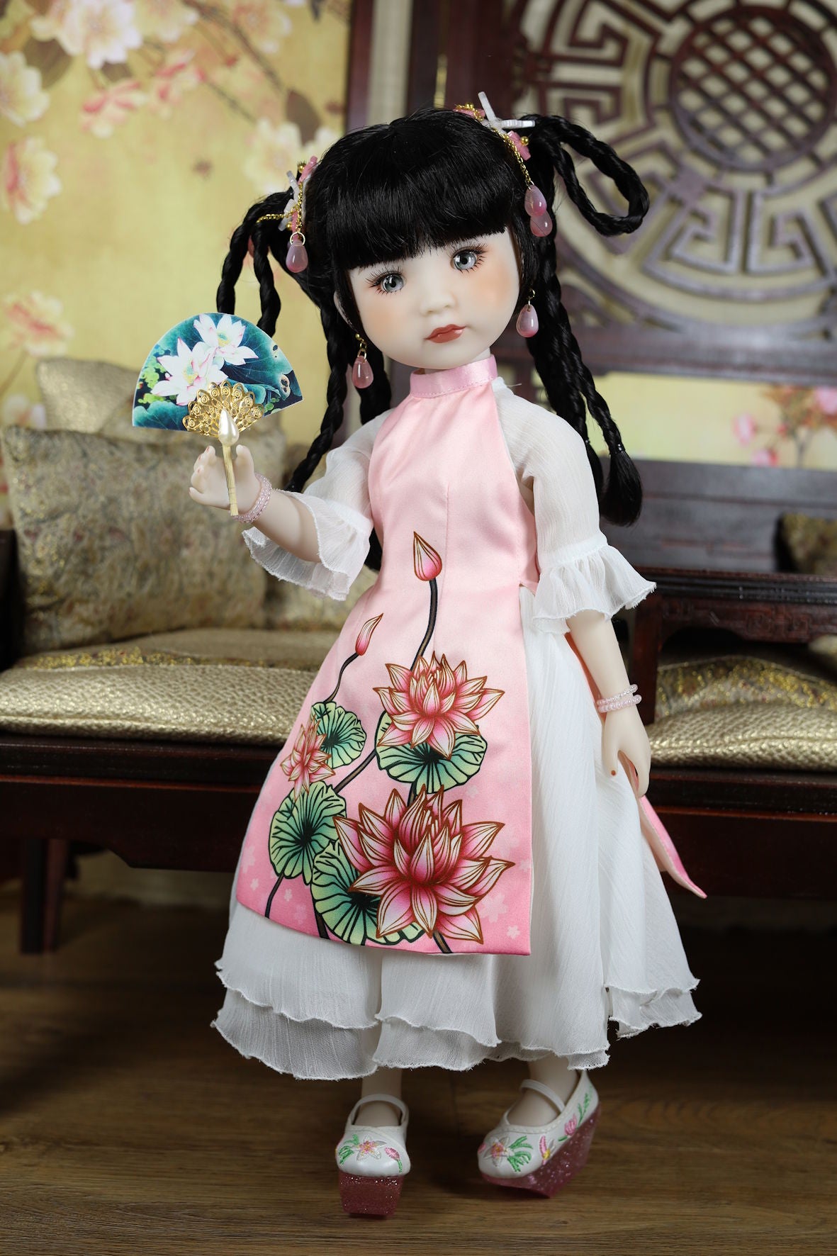 Traditional doll in a floral dress with a decorative fan, set against a decorative background.
