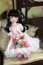 Doll in a pink dress with floral design sitting on a textured surface.