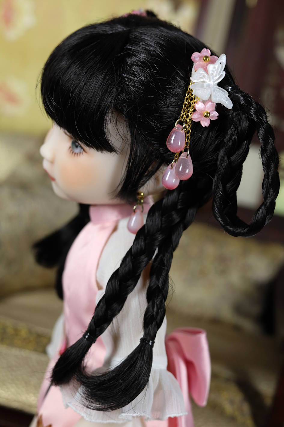 Doll with braided hair and decorative hair accessories in a blurred indoor setting