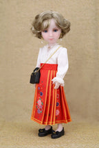 Doll wearing a red embroidered skirt and white blouse with a black handbag on a beige background