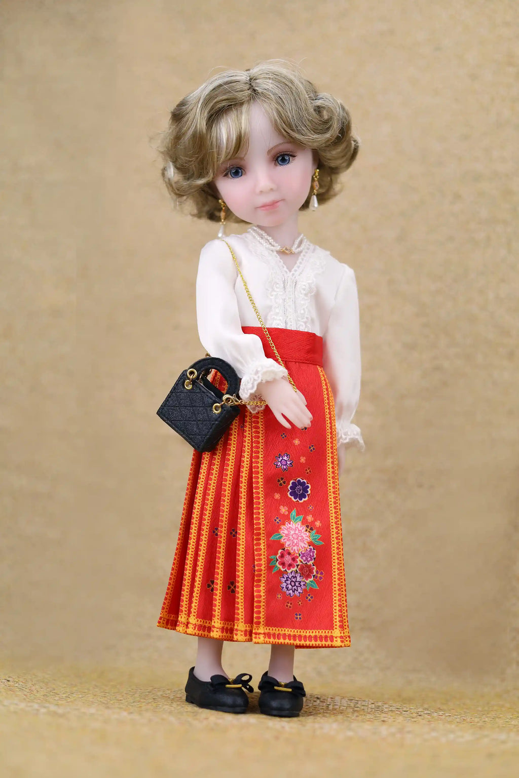 Doll wearing a white blouse and red skirt with floral embroidery on a beige background