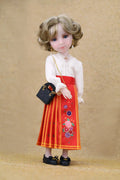 Doll wearing a white blouse and red skirt with floral embroidery on a beige background