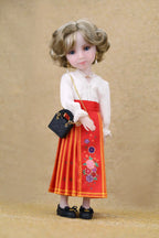 Doll wearing a white blouse and red skirt with floral embroidery on a beige background
