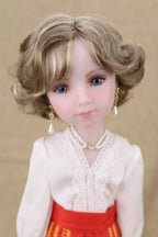 Doll with blonde hair and blue eyes wearing a white blouse and red skirt against a beige background
