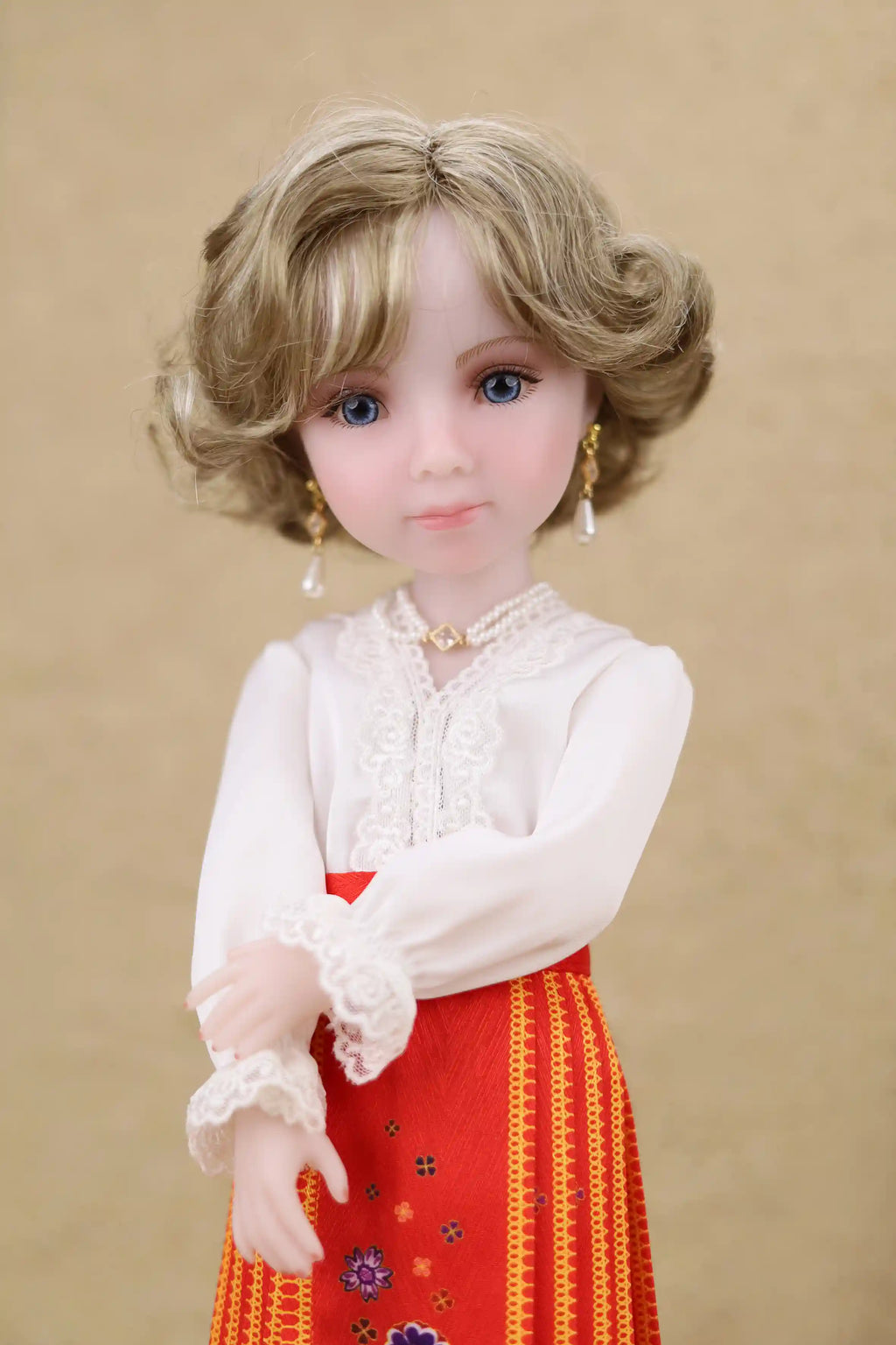 Doll with blonde hair and blue eyes wearing a white blouse and red skirt with patterns on a beige background