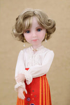 Doll with blonde hair and blue eyes wearing a white blouse and red skirt with patterns on a beige background