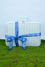 White wicker picnic basket with a blue ribbon on a grassy surface