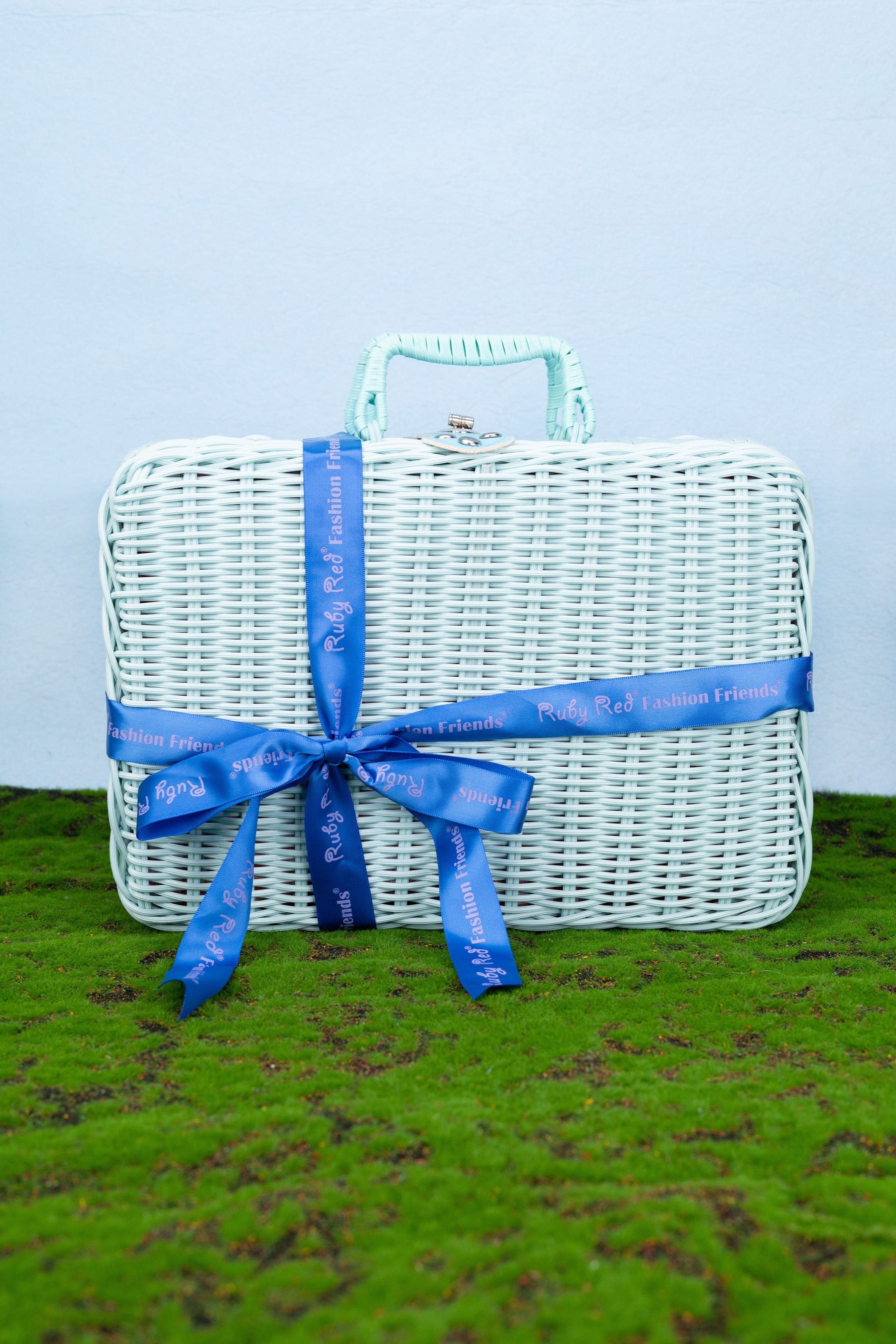 White wicker picnic basket with a blue ribbon on a grassy surface