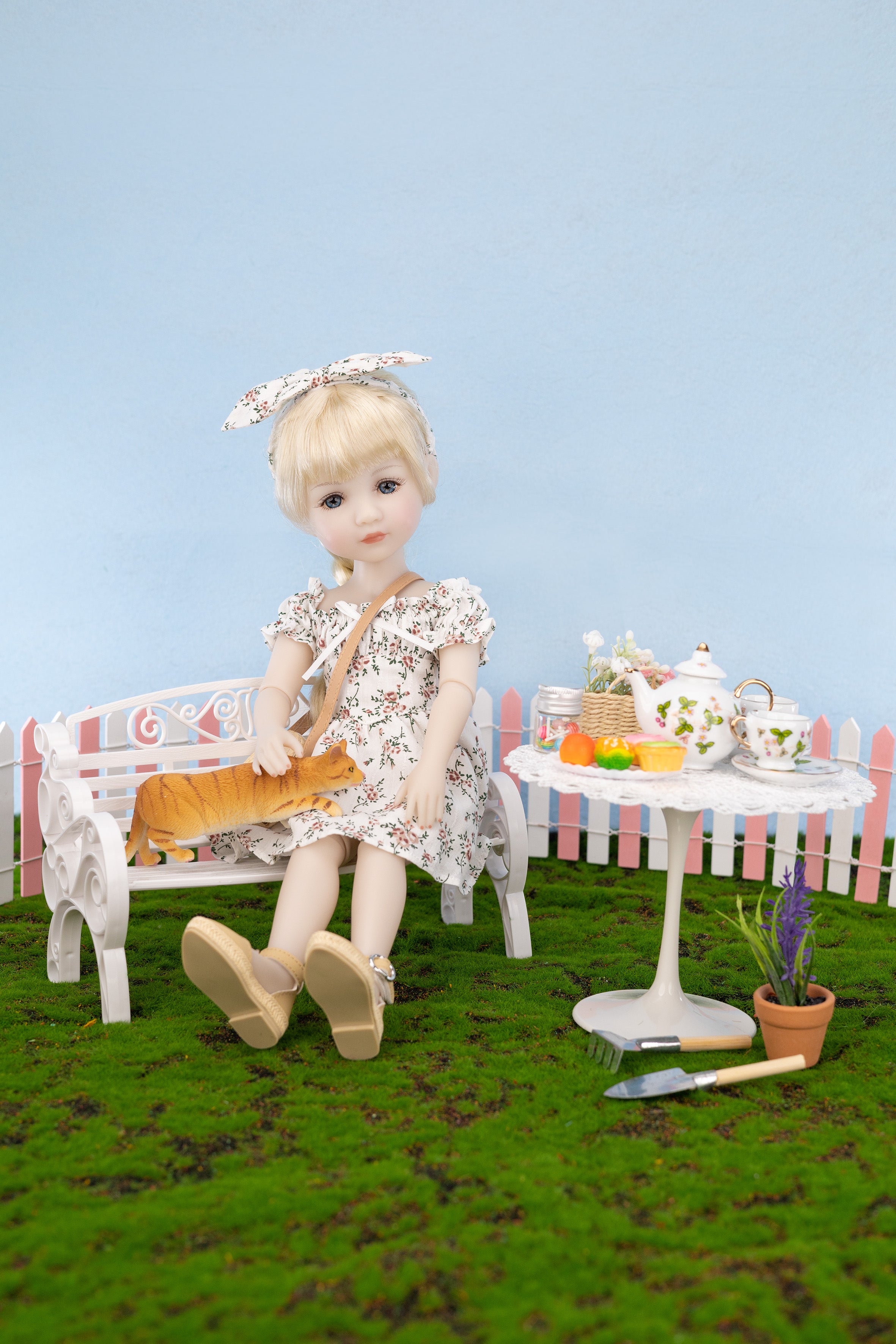 Doll sitting on a bench with a table in a garden setting