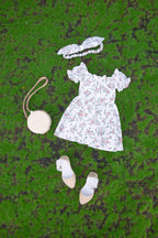 White floral dress with matching shoes, handbag, and headband on a green textured surface