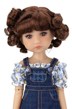 Doll with brown hair styled in buns, wearing a denim overalls and floral blouse on a white background