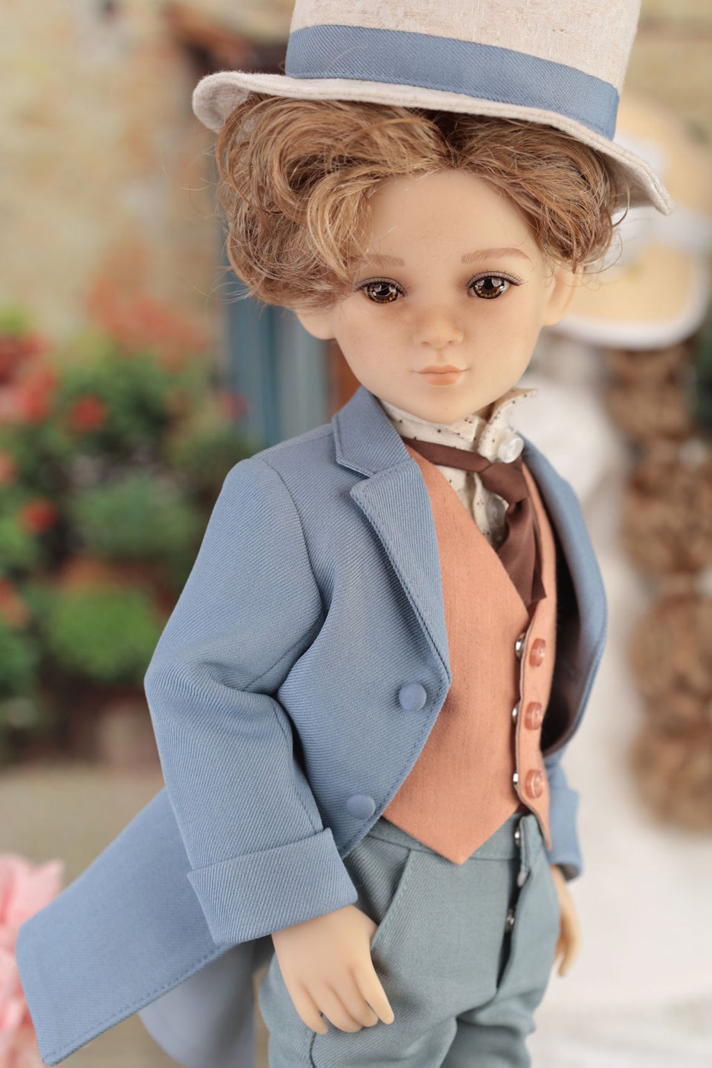Doll in a formal outfit with a blue coat and hat, standing outdoors.