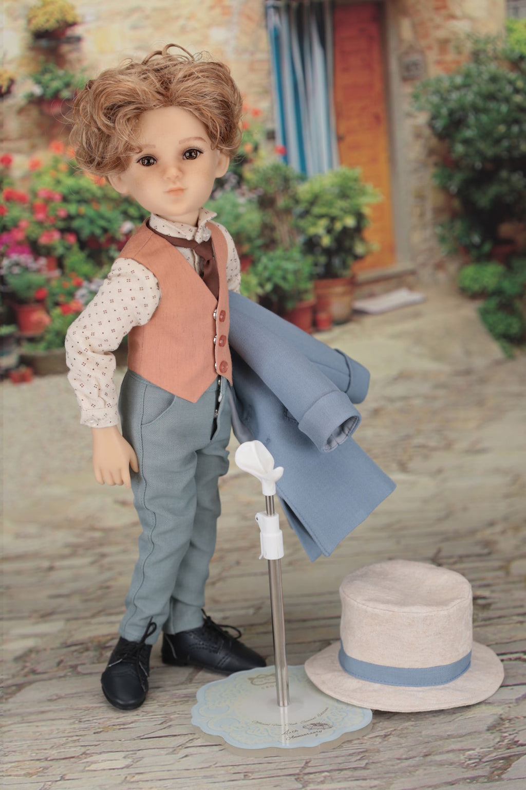 Doll in a vintage outfit with a hat and rolled-up paper on a wooden floor.