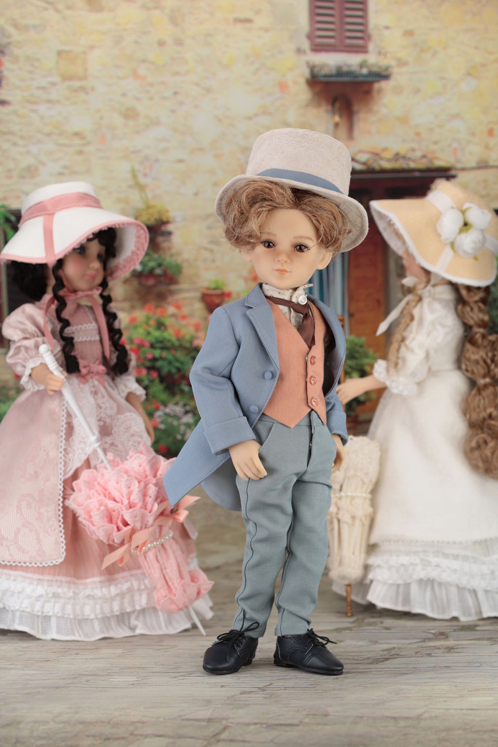 Three dolls in period costumes standing outdoors with a stone building in the background.