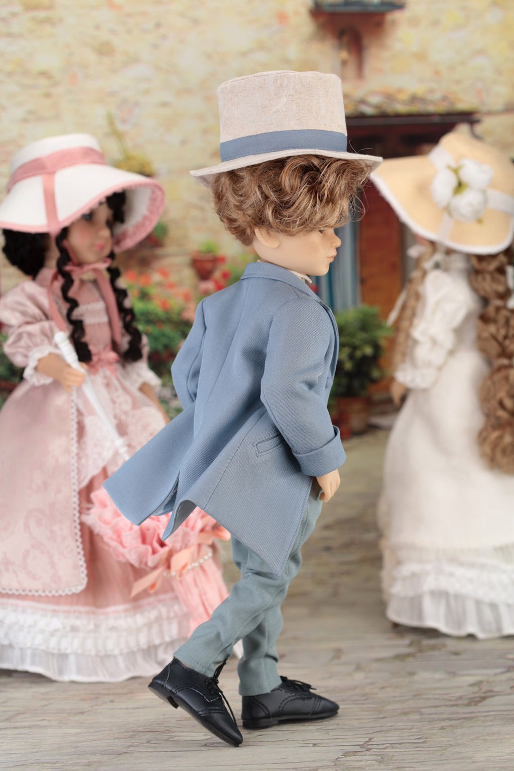 Boy doll in a formal outfit with a hat, standing in front of two dolls in vintage dresses.