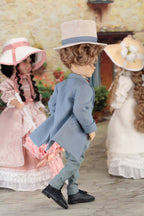 Boy doll in a formal outfit with a hat, standing in front of two dolls in vintage dresses.