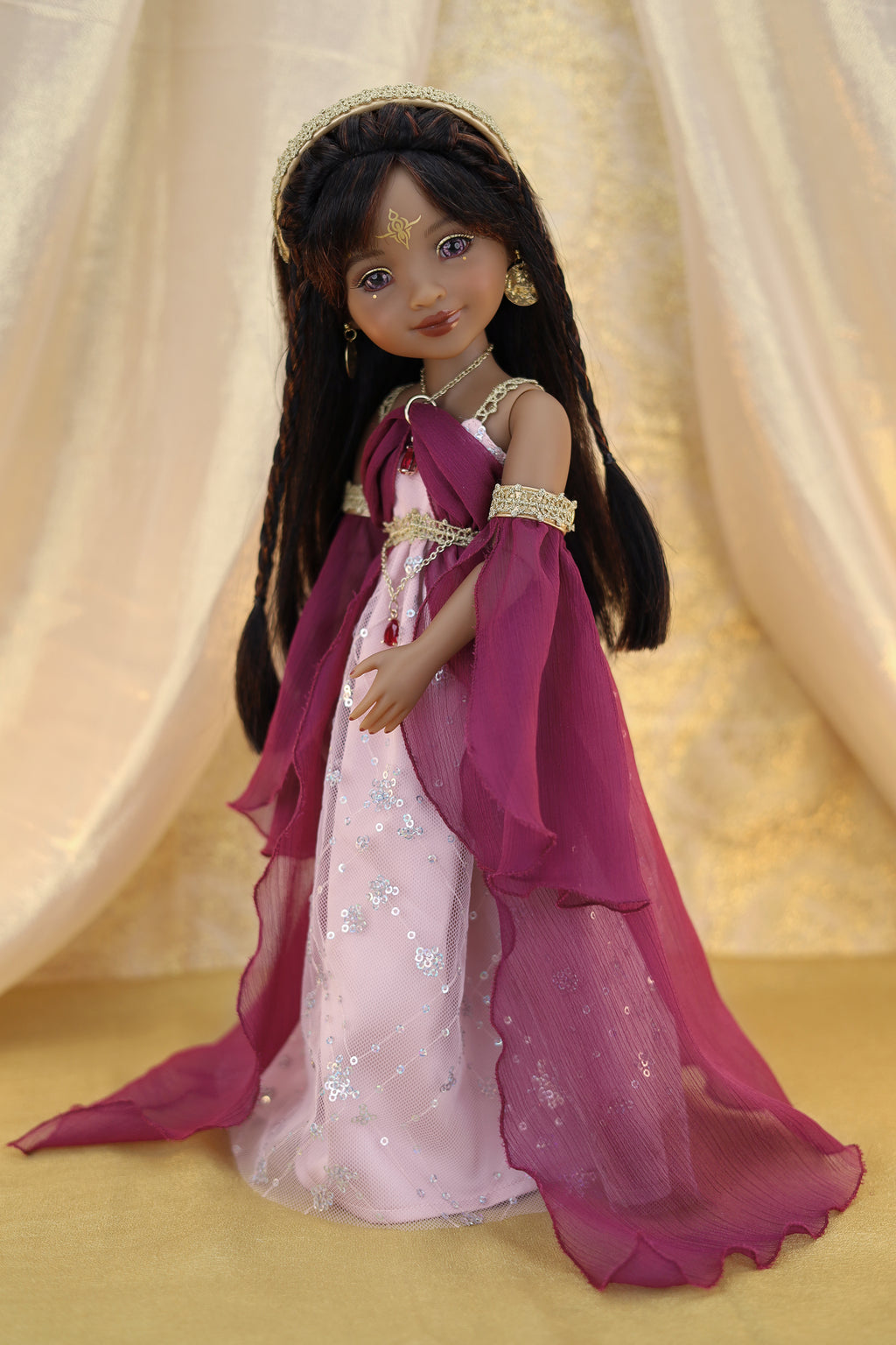 Doll in a pink and purple dress with a gold headband against a beige curtain background