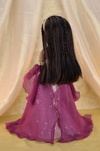 Doll with long braided hair wearing a purple outfit against a beige curtain background