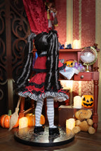 Doll in a Halloween-themed room with pumpkins, candles, and a teddy bear.