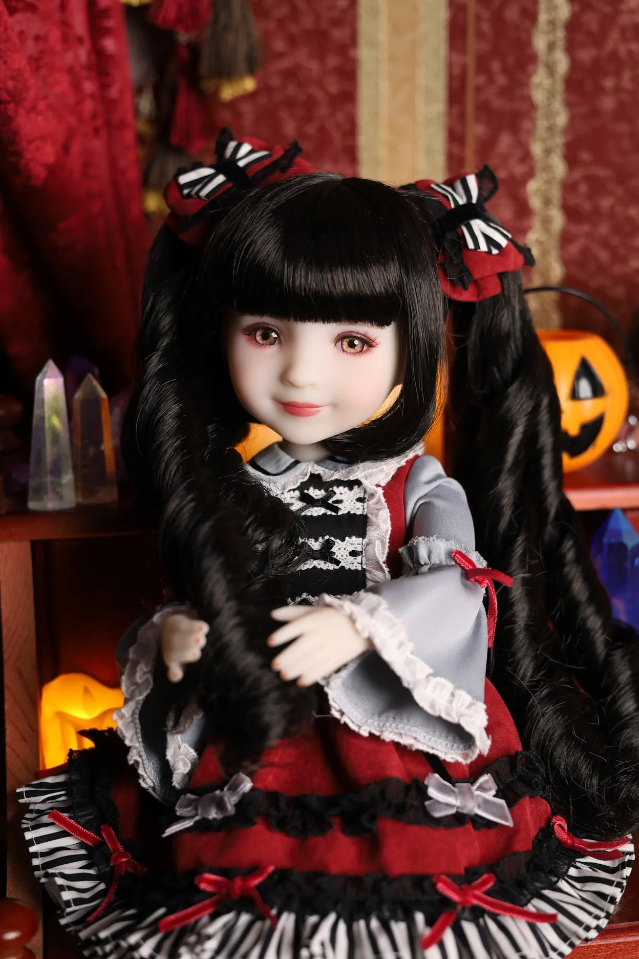 Doll with black hair and a red and black outfit in a Halloween-themed setting