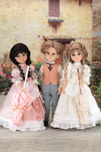 Three dolls in vintage clothing standing in front of a brick building with flowers.