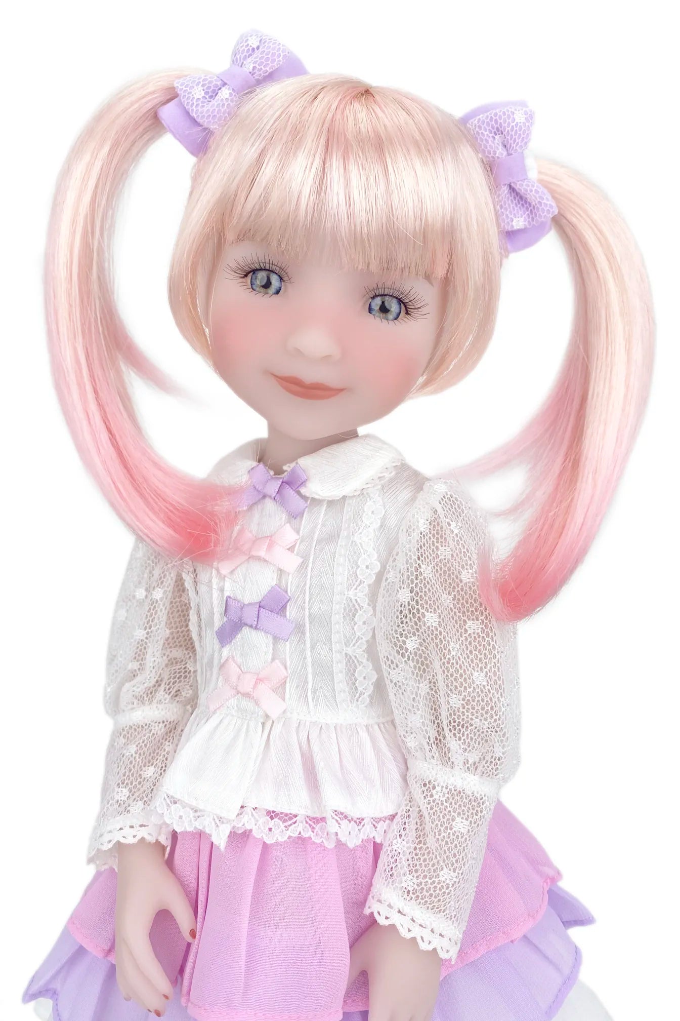 Doll with blonde hair in pigtails, wearing a white lace top and pink skirt on a white background