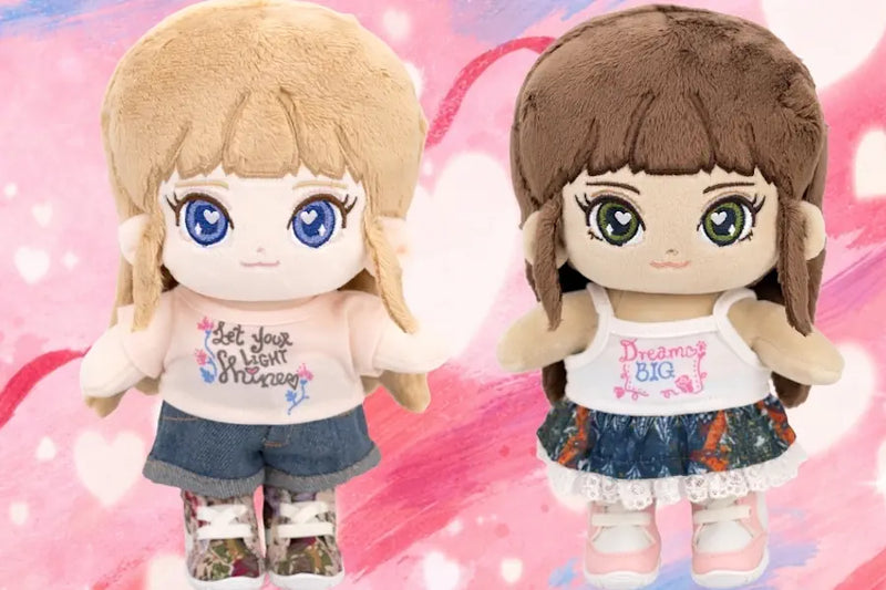 Two plush toys with anime-style designs on a pink background