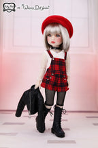Doll wearing a red beret, plaid dress, and black boots against a white background.