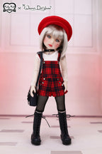 Doll wearing a red beret, plaid dress, and black boots with a blurred background