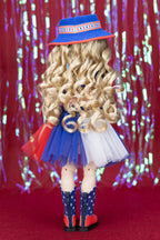 Doll with curly blonde hair wearing a blue hat, red skirt, white top, and star-patterned boots against a colorful curtain background.