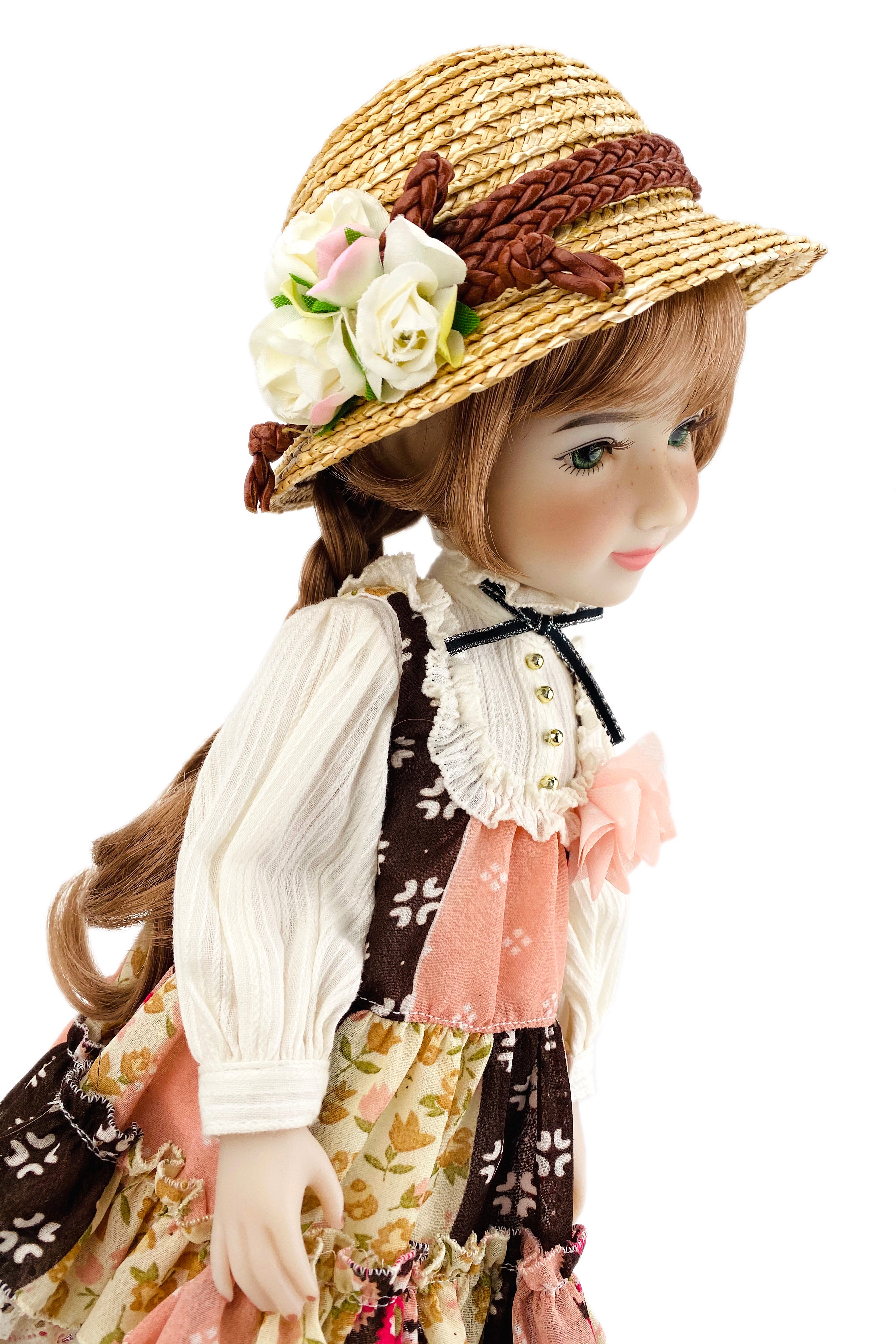 Doll wearing a straw hat with flowers and a floral dress on a white background