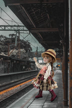 Doll in a vintage dress and hat standing on a train platform.