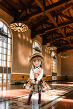 Doll in a vintage outfit standing in a grand hall with high ceilings and large windows.