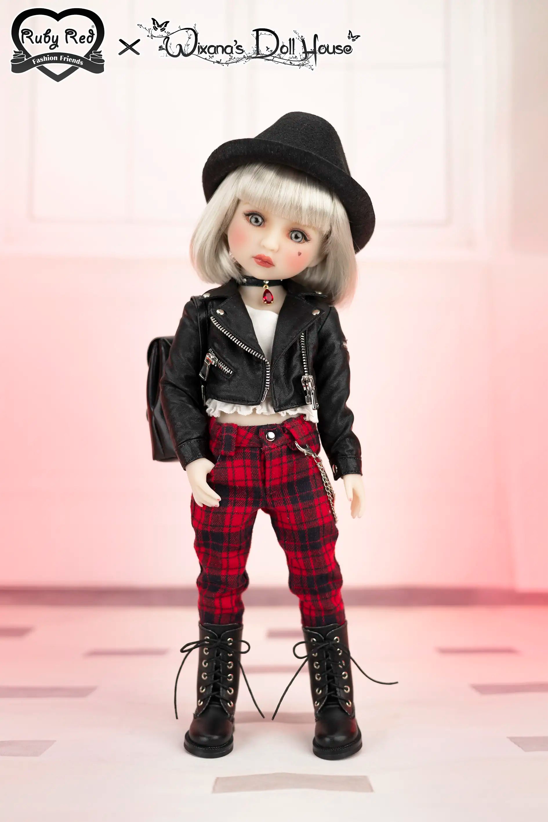 Doll wearing a black leather jacket, red plaid pants, and black hat on a pink background