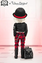 Doll wearing a black outfit with red plaid pants, black hat, and black boots, standing next to a black backpack on a pink background.