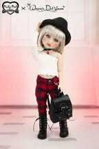 Doll with black hat, white top, red plaid pants, and black boots holding a black bag on a light pink background.