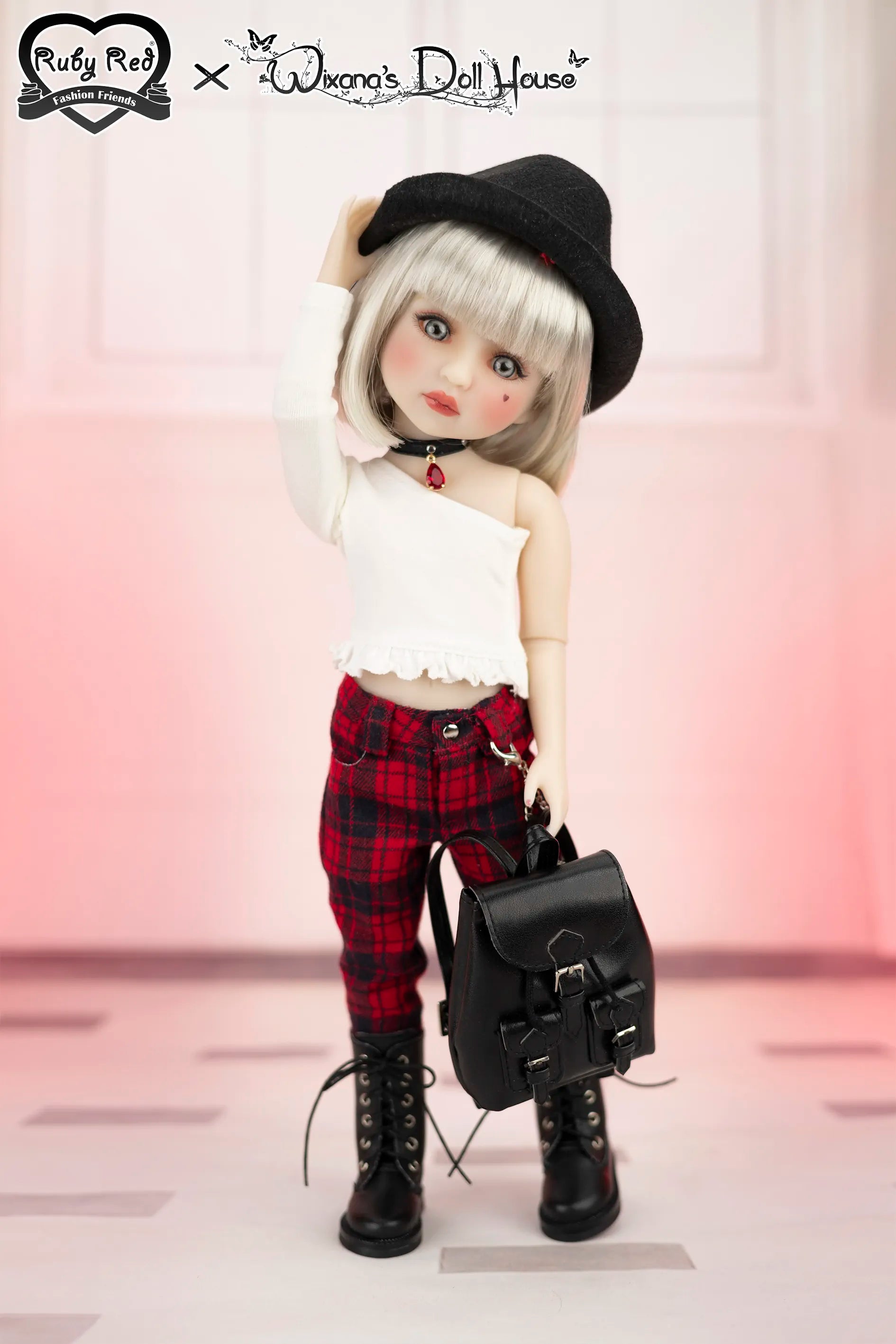 Doll with black hat, white top, red plaid pants, and black boots holding a black bag on a light pink background.