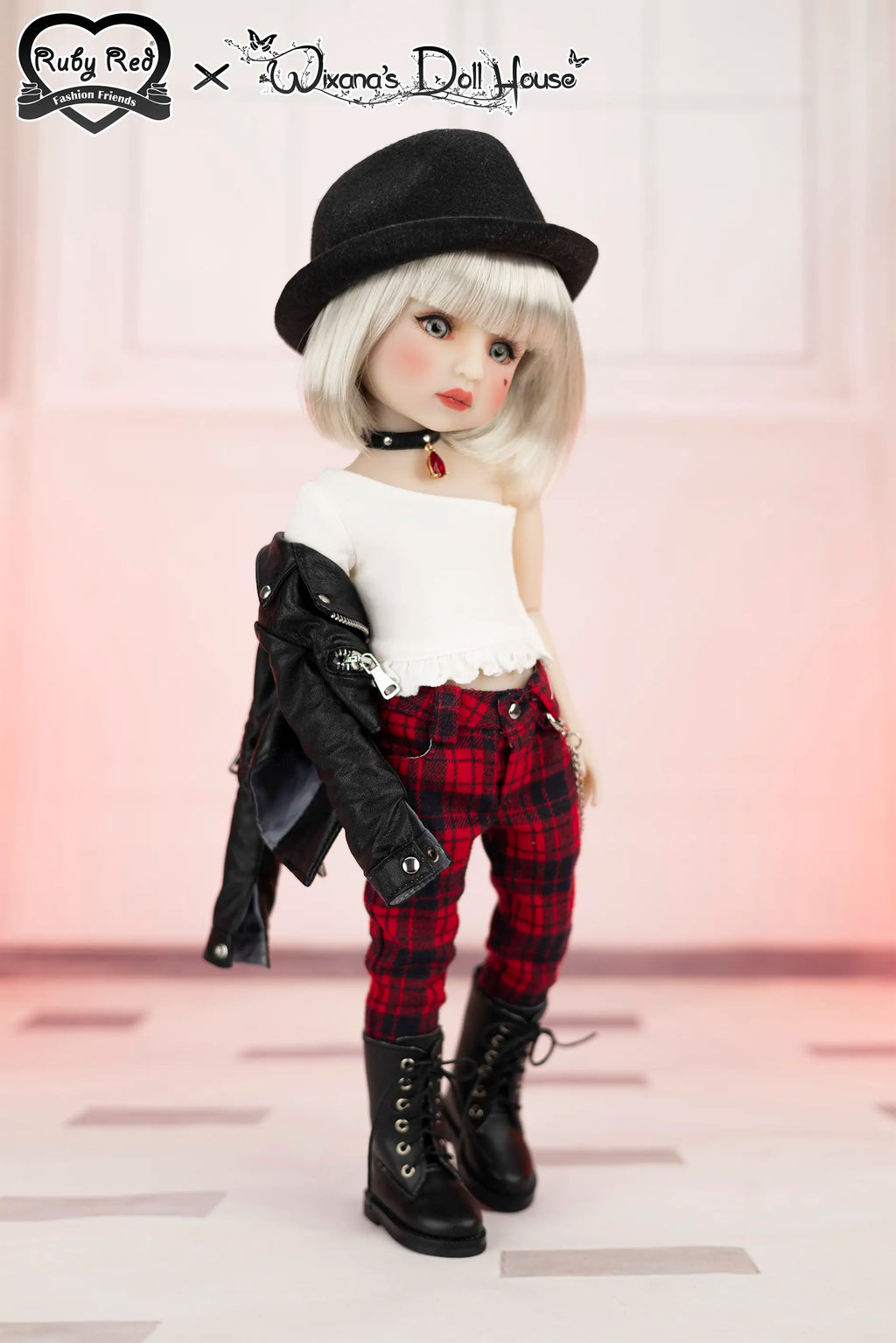 Doll wearing a black hat, white top, red plaid pants, and black boots on a light pink background.
