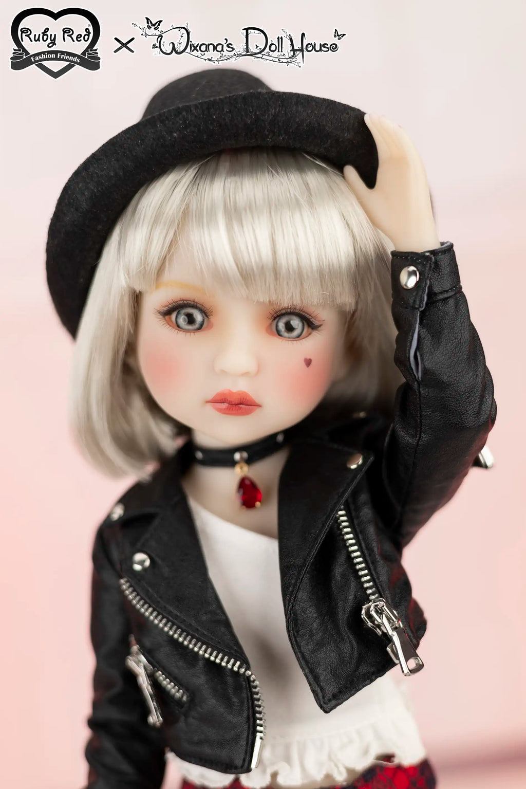 Doll wearing a black jacket and hat with a pink background